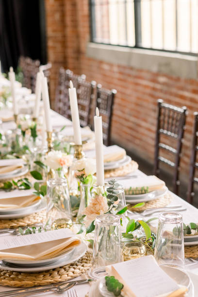 istock An elegant head table in a brick warehouse. The table is decorated with candlesticks, plates and menus, and greenery and florals. 2115826916