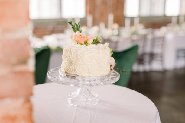 istock A simple one-layer wedding cake layered with roses and greenery on a white tabletop in a wedding reception. 2115831503