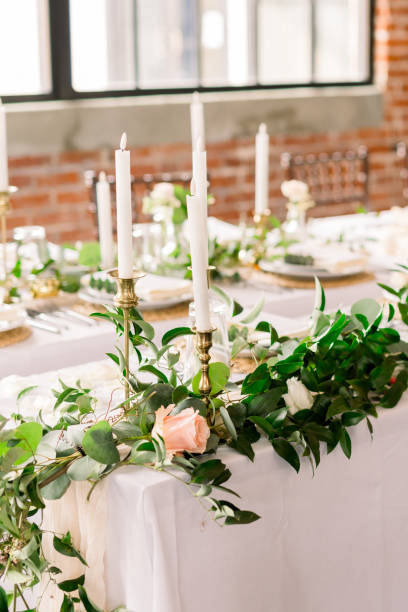 istock Long white tables set up for a wedding reception with greenery, roses, and tall candlesticks. 2115833053