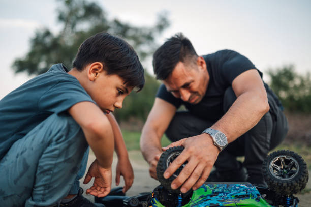 istock Dad and his boy are fixing a broken remote toy car while crouching outdoors. 2115849358
