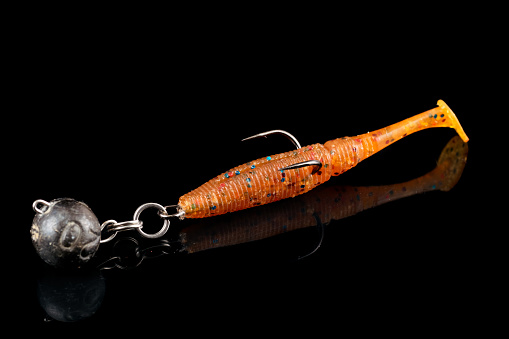 Orange fishing lure, plastic shad fish, with double hook and lead sinker, isolated on black background