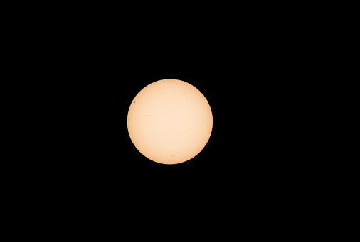 Orange sun with black sunspots visible against black background