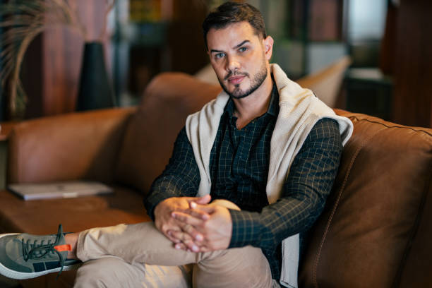 istock Young man sitting on the couch and looking at camera 2115899408