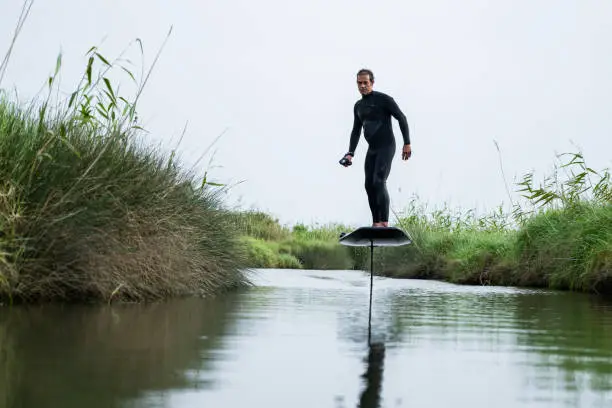 Hydrofoil rider gliding over the water with his board in one of the canals of the Ria de Aveiro in Portugal on a cloudy day.