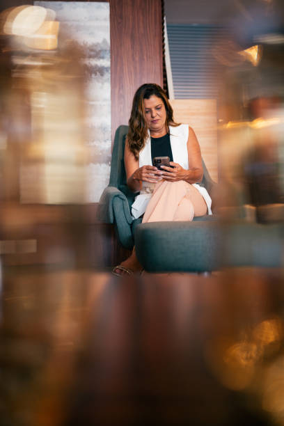 istock Beautiful woman sitting on the couch and using cell phone 2115930971