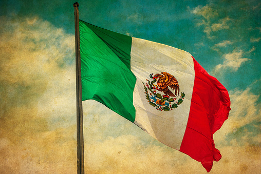 Grunge image of Mexico flag over blue cloudy sky