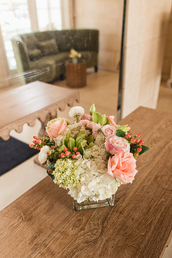 Pink Rose & Hydrangea Arrangement in a Vase on top of a Scalloped Table with a Rich Green Couch in the Background  in Palm Beach, Florida in March of 2024