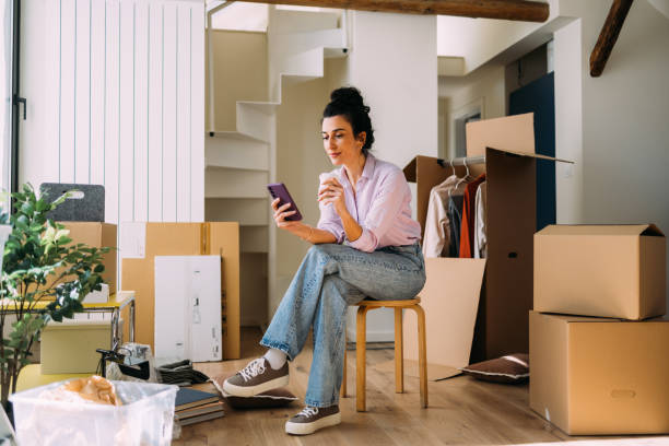 istock Young Woman Using Smartphone During Moving Day at New Home 2115959775