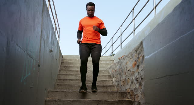 Man, fitness and running on steps outdoor for exercise, cardio workout and sports training. African runner, urban performance and action on stairs for energy, wellness and strong endurance challenge