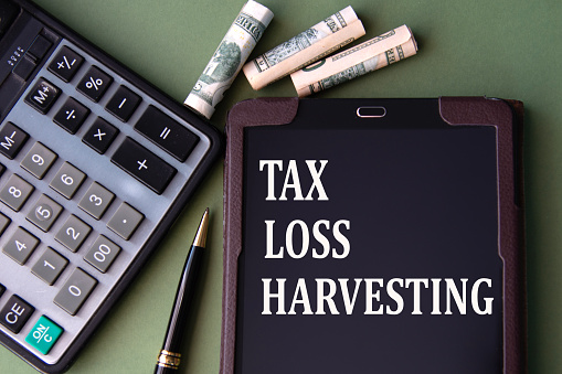 TAX LOSS HARVESTING - words in an electronic notebook on the background of a calculator and banknotes