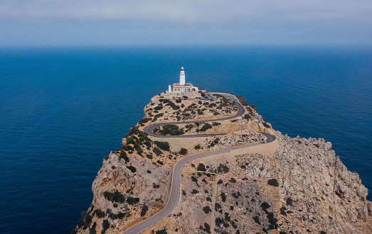 Lonely Lighthouse at Cap de Formentor with serpentine curved asphalt mountain road with breathtaking Mediterranean seascape. Majorca Island, Balearic Islands, Spain. Aerial drone point shot.