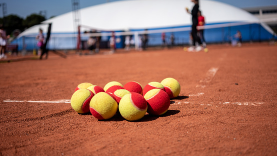 red tennis balls are on clay court children and coach are ackground focus on foreground horizontal still