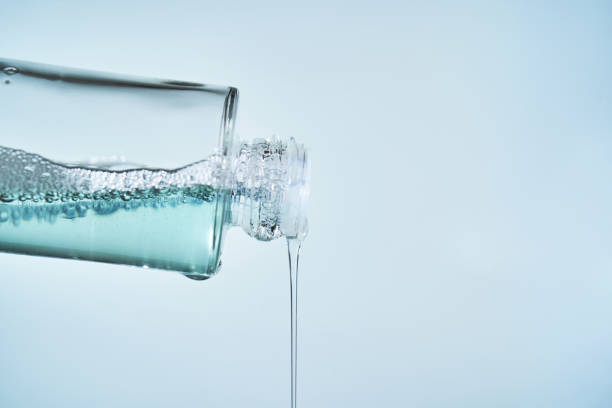 Cosmetic bottle from which serum is pouring on a blue background.