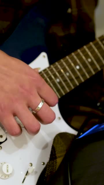Close-up shot of a guitarist strumming a blue guitar in a small studio