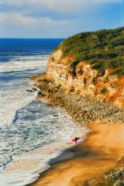 surfer mit rotem surfbrett am bells beach, great ocean road, victoria, australien - australian culture landscape great ocean road beach stock-fotos und bilder