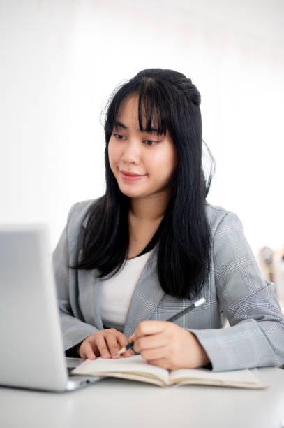 istock A young Asian businesswoman is looking at her laptop screen while taking notes in the notebook. 2116216925