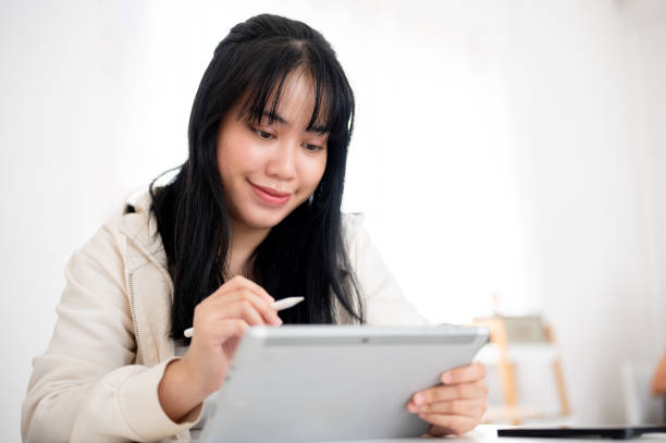 istock A young Asian woman using her digital tablet with a stylus pen at a table indoors. 2116217452