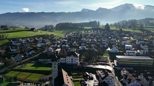 Benken, switzerland with buildings, green areas, and clear skies, sunlight casting shadows, aerial view