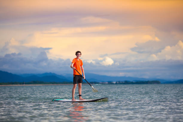 Young man on stand up paddle board. Water fun and beach sport. Healthy outdoor sports for summer vacation on tropical island. Holiday activity. Fit teenager boy training. Surfer exercising.