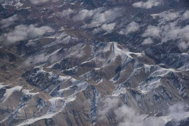 This image is of a snowy mountain with a glacier located in northern China, just south of the city of Urumqi. The image was taking from the window of an aircraft at 34,000 feet. The photos is an aerial view of snow-covered mountain peaks and glaciers in a rugged alpine landscape. Jagged ridges and steep slopes rise dramatically above deep valleys, with contrasting textures of ice, rock, and snow under clear daylight. The remote and pristine scenery highlights the raw beauty of high-altitude terrain of northern China.