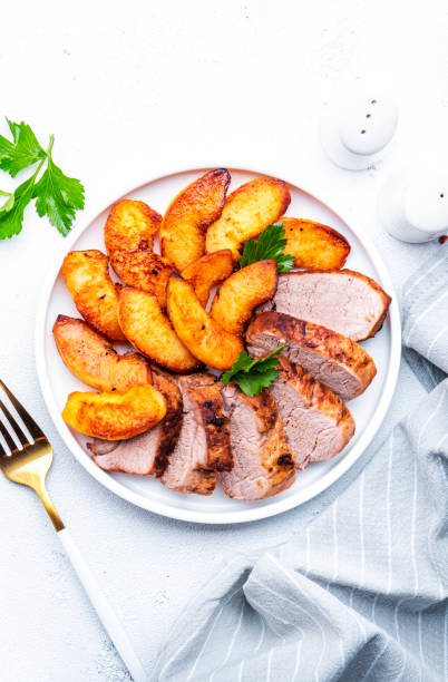 istock Baked pork tenderloin with caramelized apples on plate, white table background, top view 2116387517
