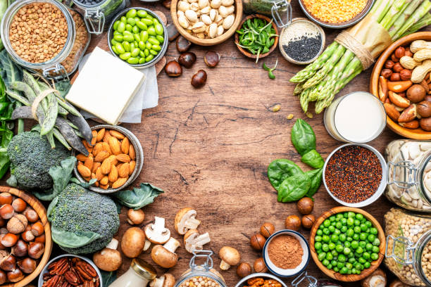 istock Vegan food background with empty space., frame. Plant protein., vegetarian nutrition sources. Healthy eating, diet ingredients: legumes, beans, lentils, nuts, soy milk, tofu, cereals, seeds and sprouts. Top view, wooden table 2116387540