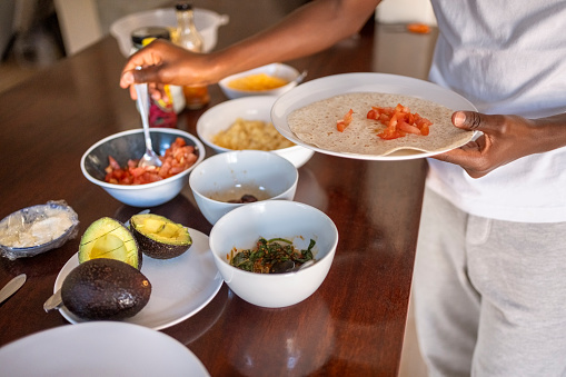 Cropped shot of teenage boy taking food in his plate from breakfast table in morning at home