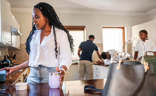 African woman making a coffee with family in background in kitchen at home