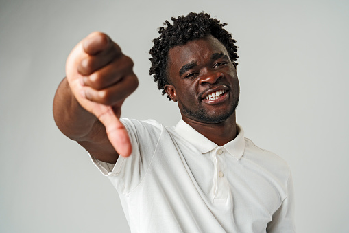 Young African Man Giving Thumbs Down Gesture Against a Neutral Background in Studio