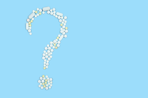 medicinal pills laid out in the form of a question mark on a blue background