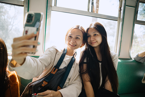 Happy Asian mother and daughter taking selfie in the train while traveling