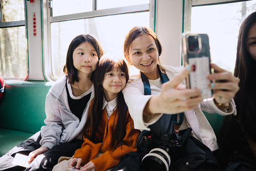 Happy Asian mother and daughters taking selfie in the train while traveling