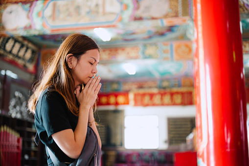 Asian woman praying and making a wish in chinese temple
