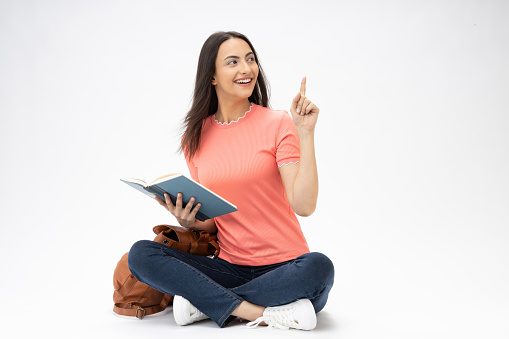 Full length body size photo of young girl reading book sitting on floor wearing jeans denim pink t-shirt footwear isolated over white background