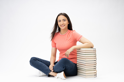 Full length body size photo of young girl book stack relaxation sitting on floor wearing jeans denim pink t-shirt footwear isolated over white background