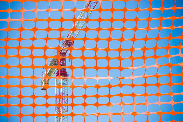 Construction site with safety plastic orange grid against a tower crane.