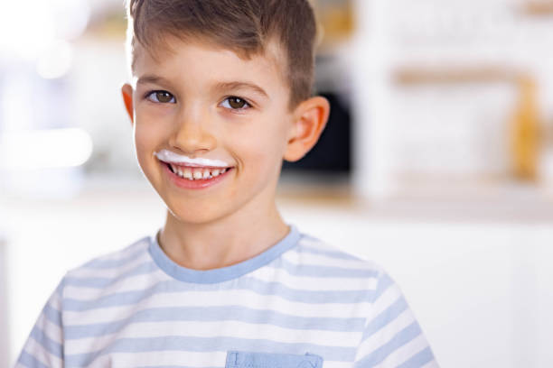 Portrait of cute boy having yogurt mustache in dining room and looking at camera.