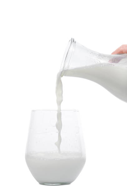 istock Fresh milk poured from a glass jug into a glass on a white background 2116581124
