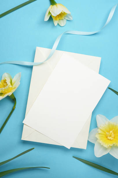 istock Invitation or greeting card mockup with fresh daffodils flowers on a blue background. Top view, flat lay. Space for text. Blank card mock up. 2116603403
