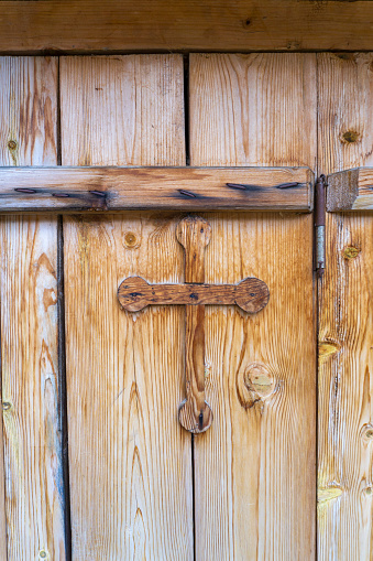 Old wooden door with a wooden cross. Wooden strip nailed with rusty nails near the door hinge. Wood texture are visible.