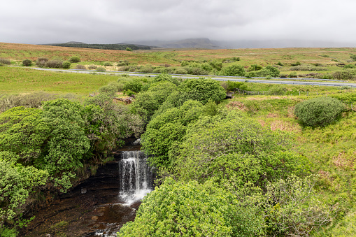 Nestled in lush greenery, the Lealt Falls create a tranquil haven on Isle of Skye, complemented by a countryside road and the distant