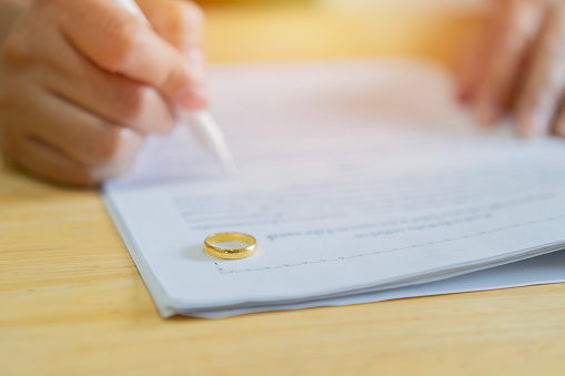 Hands of wife, husband signing decree of divorce, canceling marriage or premarital agreement prepared by lawyer. Selective focus on ring.