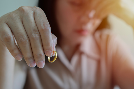 Closeup of a single sad wife after divorce lamenting holding the wedding ring in room at home. Selective focus.