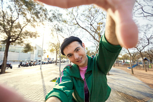 Waist-up view of playful 21 year old in green and pink tracksuit placing hands around photographer’s lens and smiling at camera.