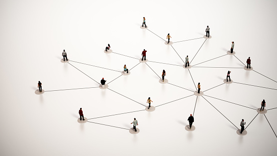 An arrangement of miniature human figures stands on a bright white backdrop, interconnected by thin black lines that simulate a network or a web of social or professional relationships. The figures vary in posture and orientation, suggesting dynamic interaction or communication paths within a simplified model of a community or organization structure.