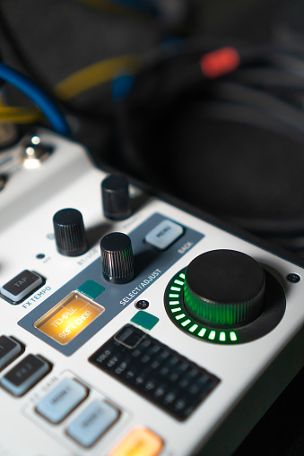 Close-up image of hand adjusting mixer knob for volume control during live studio performance. Mixer features multiple knobs and buttons for precise audio mix adjustments. Vertical photo