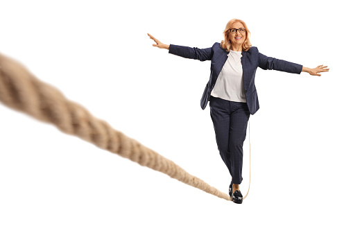 Full length portrait of a middle aged woman walking on a rope isolated on white background