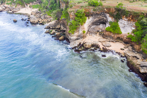 Rocky shoreline adorned with green vegetation contrasts the clear blue water. The aerial view captures sandy beaches, rock formations, and the serene ocean.