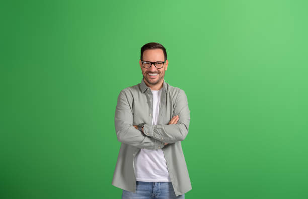 istock Young handsome freelancer in glasses smiling at camera and standing confidently on green background 2116729740