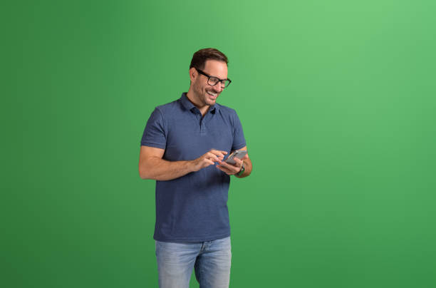 istock Handsome young man in glasses smiling and checking messages over mobile phone on green background 2116730251
